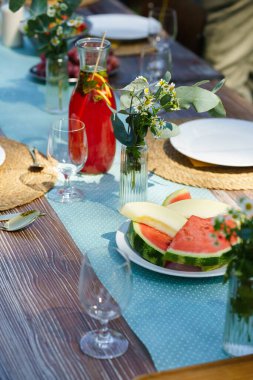 Bir yaz bahçe partisinde sehpanın yakın çekimi. Bardaklı masa, limonata, taze meyve limonatası ve çiçekli süsleme..
