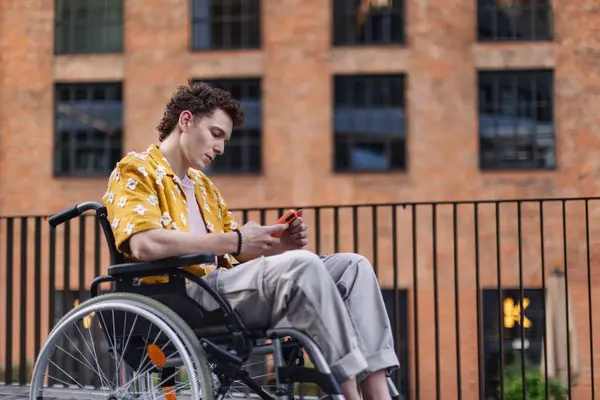 Gen Z boy in a wheelchair in the city using smartphone. Inclusion, equality, and diversity among Generation Z.
