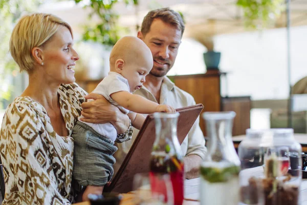 Family with little baby in a restaurant, choosing food and drinks. Family dinner at a restaurant.