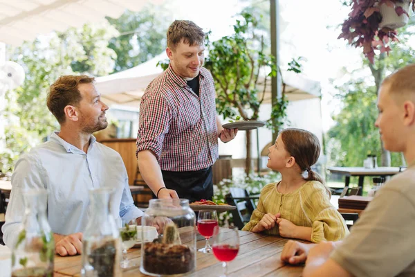 Waiter bringing food to the table in the restaurant. Family having dinner at a restaurant.