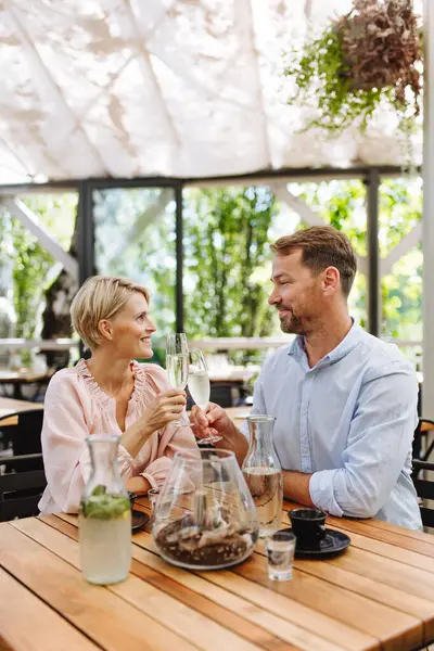 Portrait of beautiful couple in a restaurant, on a romantic date. Husband and wife are clinking champagne glasses, making a toast at restaurant patio.