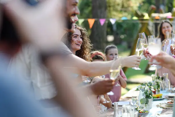 Group of friends clinking glasses at garden party. Celebratory toast at the party table.