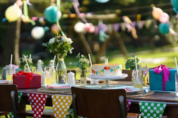Wide shot of the birthday table with colorful decorations, birthday cake, and gifts. Inspiration for simple, tasteful birthday decoration for a garden party.