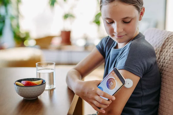 Girl with diabetes checking blood glucose level at home using continuous glucose monitor. Schoolgirl connecting CGM to a smartphone to monitor her blood sugar levels in real time.