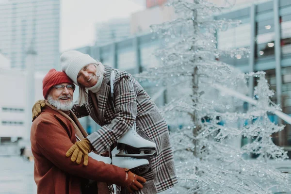 Portrait of seniors in winter at an outdoor ice skating rink. Beautiful elderly woman and man holding new ice skates.
