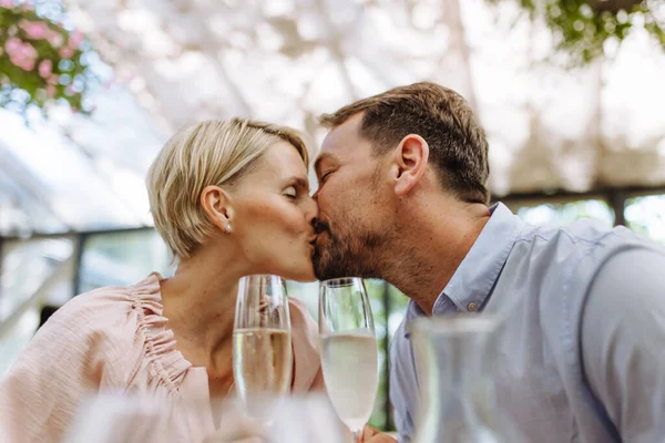 Close up of beautiful couple in a restaurant, on a romantic date. Wife and husband kissing, having a romantic moment at restaurant patio.