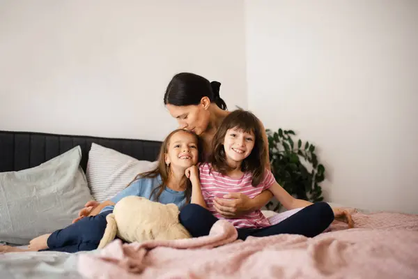 ベッドルームのベッドに2人の娘がいる母親の肖像 父親のいない家族が座って抱き合う 母の日と母の愛の概念 — ストック写真