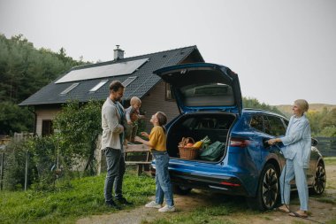 Çatıda güneş panelleri olan elektrikli arabalı bir aile evlerinin önünde duruyor. Güneş enerjisi ve genç bir ailenin sürdürülebilir yaşam tarzı. Yeşil enerji kavramı ve gelecek için sürdürülebilir gelecek