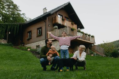 Çatıda güneş panelleri olan bir aile evlerinin önünde duruyor. Güneş enerjisi ve genç bir ailenin sürdürülebilir yaşam tarzı. Yeşil enerji kavramı ve gelecek nesiller için sürdürülebilir gelecek.