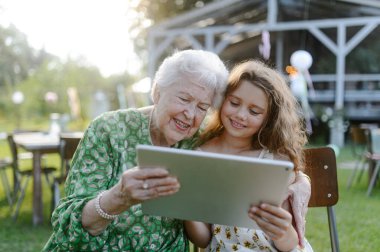 Bir bahçe partisinde yaşlı büyükanneme tablette bir şey gösteren genç bir kız. Büyükbaba ve torun arasındaki sevgi ve yakınlık.