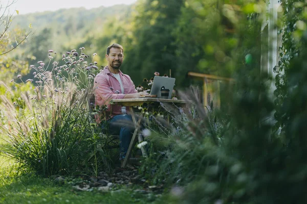 Man working in garden, with laptop on legs. Businessman working remotely from outdoor homeoffice, thinking about new business or creative idea.
