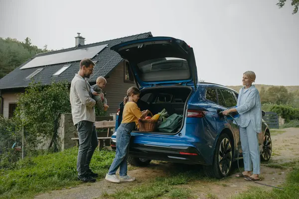 Çatıda güneş panelleri olan elektrikli arabalı bir aile evlerinin önünde duruyor. Güneş enerjisi ve genç bir ailenin sürdürülebilir yaşam tarzı. Yeşil enerji kavramı ve gelecek için sürdürülebilir gelecek