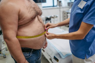 Kadın doktor, kilolu hastanın belini mezurayla ölçüyor. Obezite orta yaşlı erkeklerin sağlığını etkiliyor. Aşırı derecede obezite ve sağlık riskleri kavramı.