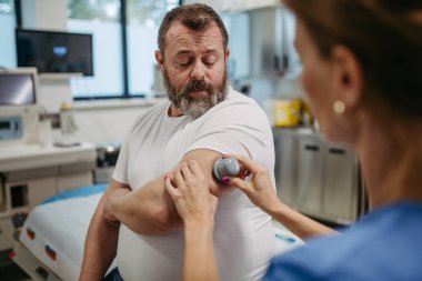 Doktor hasta koluna sürekli glikoz monitörü takıyor. Obez ya da kilolu bir adamın tip 2 diyabet olma riski var. Aşırı derecede obezite ve sağlık riskleri kavramı.