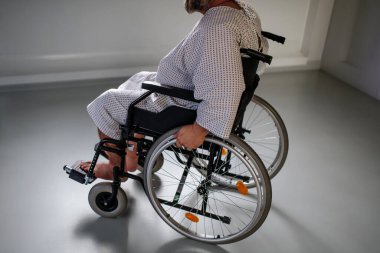 Tekerlekli sandalyedeki adamın yan görüntüsü. Hastane önlüklü şişman hasta hastanede muayene için bekliyor..