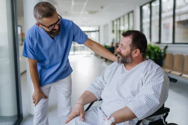 Tekerlekli sandalyedeki endişeli şişman hastayla destekleyici doktorların konuşmalarını kapatın. Orta yaşlı erkek sağlığında hastalıklar ve hastalıklar. Stresli hastayı destekleyen şefkatli bir doktor. Konsept