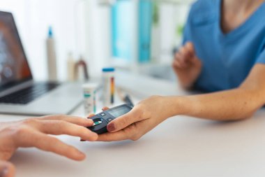 Diabetologist doctor testing blood sample on blood sugar meter in diabetes clinic. Doctor taking blood sample from boys finger. Paediatric diabetes in teenage boy, young man. clipart