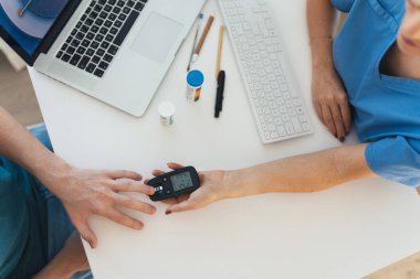 Diyabetolog doktor kan örneğini diyabet kliniğinde glukometre üzerinde test ediyor. Doktor oğlanların parmağından kan örneği alıyor. Genç çocukta pediatrik diyabet, genç adam..
