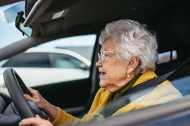 Tek başına araba süren mutlu, araba yolculuğunun tadını çıkaran son sınıf kadını. Yaşlı yetişkinler için güvenli sürüş, yaşlı sürücünün güvenliği. Yaşlanınca ehliyet yenileme.