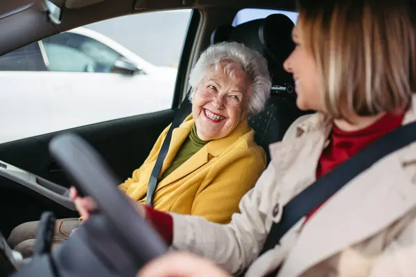 Granddaughter driving her elderly grandmother in the car, taking her to the doctor, shopping or to bank. Caregiver driving elderly lady to the church, pharmacy.