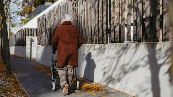 Senior woman with a mobility walker walking alone on the city streets during autumn day, feeling lonely.
