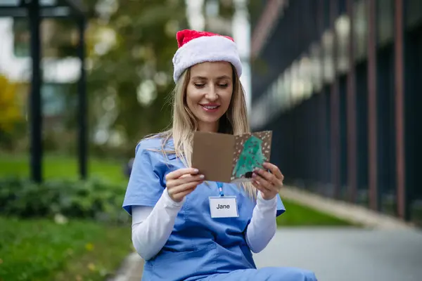 Nurse with christmas hat on head reading christmas card from child patient. Working in hospital on Christmas day. Female doctor working a Christmas shift and cant be with her family.