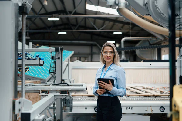 Portrait of female engineer standing in modern industrial factory. Manufacturing facility with robotics and automation. Female leader, CEO in heavy industry, manufactury.