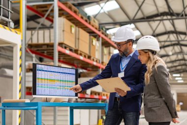 Rear view of female engineer and male project manager standing in modern industrial factory, talking about production. Team management in manufacturing facility clipart