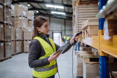 Female warehouse worker holding scanner and scanning the barcodes on products in warehouse. Warehouse manager using warehouse scanning system. clipart