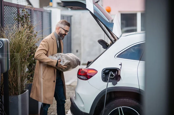 Man Putting Bag Wood Pellets Car Trunk While His Electric — Stock Photo, Image