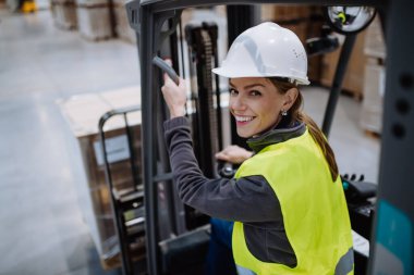Forklift kullanan kadın depo işçisinin portresi. Depo işçisi nakliye, teslimat ve depodaki stokları kontrol etmek için ürünler hazırlıyor..