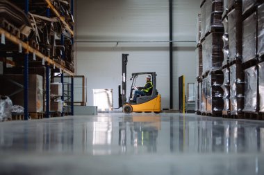 Depoda erkek şoförle birlikte forklift yan görüntüsü. Depo işçisi nakliye, teslimat ve depodaki stokları kontrol etmek için ürünler hazırlıyor..