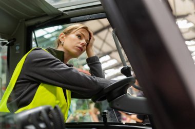 Kadın forklift sürücüsü işin yoğunluğundan bunalmış. Bitkin, bitkin bir depo çalışanı nakliye, teslimat, depodaki stokları kontrol etmek için ürünler hazırlıyor..