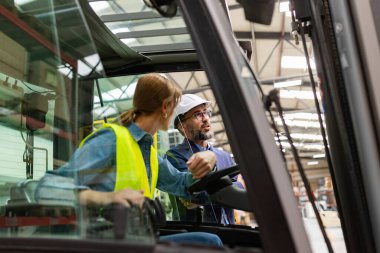 Kadın forklift sürücüsü modern endüstriyel fabrika müdürüyle konuşuyor. Depo görevlisi danışma emri, sipariş toplama. Depo çalışanı nakliyat, teslimat ve stokları kontrol etmek için ürün hazırlıyor.