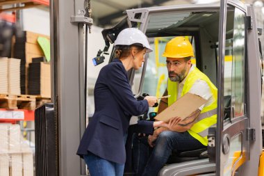 Erkek forklift sürücüsü modern endüstriyel fabrika müdürüyle konuşuyor. Depo görevlisi okuma emri, sipariş toplama. Depo çalışanı nakliyat, teslimat ve stokları kontrol etmek için ürün hazırlıyor.