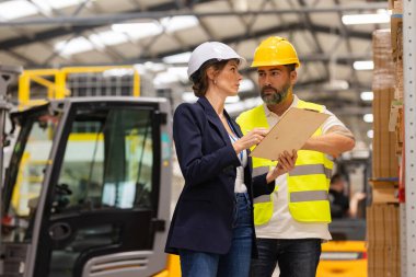 Erkek forklift sürücüsü modern endüstriyel fabrika müdürüyle konuşuyor. Depo görevlisi okuma emri, sipariş toplama. Depo çalışanı nakliyat, teslimat ve stokları kontrol etmek için ürün hazırlıyor.