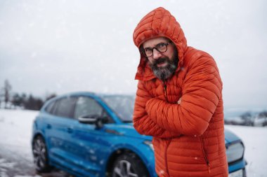 Elektrikli arabanın yanında duran kızgın adam, varış noktasına varmadan önce şarjı bitiyor, karlı kış gününde. Hüsrana uğramış bir adam yardım bekliyor, servis arabası, çekici..