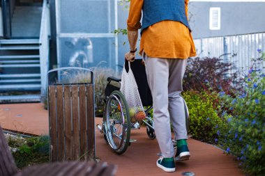 Yaşlı adam kendi tekerlekli sandalyesini itiyor. Yaşlılar için destek ve denge için tekerlekli sandalye yürüme zorluğu ve hareketlilik yardımı.