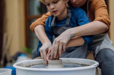 Anne oğluna çanak çömlek üzerinde nasıl çömlek yapılacağını öğretiyor. Çocuk yaratıcı aktiviteler ve sanat. Çocuk çömlek yapıyor, annenle eğleniyor. Mutlu aile anları.