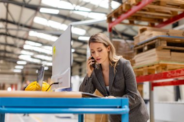 Kadın mühendis, şirket müdürü, modern endüstriyel fabrikanın yöneticisi akıllı telefondan arama yapıyor. Bilgisayar imalatında PC ile Üretim Kontrol Merkezi.