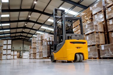 Deponun ortasında bir forklift var. Forklift sürücüsü nakliye, teslimat ve depodaki stokları kontrol etmek için ürünler hazırlıyor..