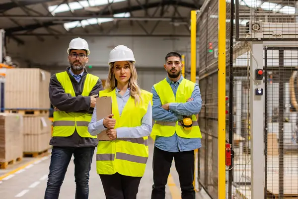 Portrait of team of warehouse employees standing in warehouse. Team of workers and female manger in modern industrial factory, manufactrury. Concept of team management.