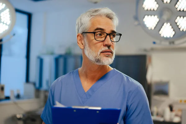 Portrait of handsome male doctor in scrubs. ER doctor examining patient, reading medical test, lab results in clipboard. ER with patient with life threatening health problems.