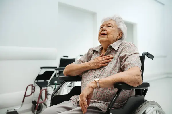 Senior woman with heart attack feeling chest pain. Elderly patient with chest pain have trouble with breathing. Patient in wheelchair in emergency room have panic attack.
