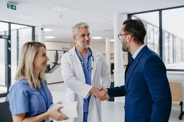 Pharmaceutical sales representative talking with doctors in medical building, shaking hands. Drug rep presenting new pharmaceutical product, drug. Hospital director, manager in private medical clinic