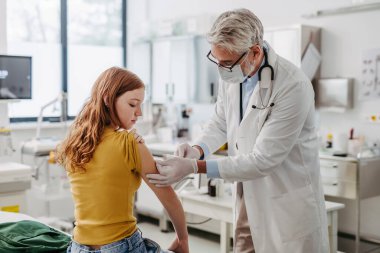 Doktor, çocuk doktoru genç kız koluna aşı enjekte ediyor, rutin aşılar. Ergenler için önleyici sağlık hizmetleri kavramı.
