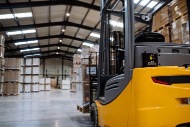 Deponun ortasında bir forklift var. Forklift sürücüsü nakliye, teslimat ve depodaki stokları kontrol etmek için ürünler hazırlıyor..