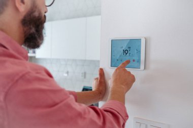 Adam akıllı termostat kullanıyor, evindeki ısıyı ayarlıyor ya da düşürüyor. Ev ısıtma ve termostatlarında sürdürülebilir, verimli ve akıllı teknoloji kavramı.
