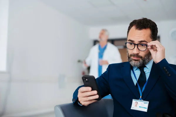 Pharmaceutical sales representative sitting in medical building, waiting for the doctor, presenting new pharmaceutical product. Male drug rep sitting in hall scrolling on smartphone.