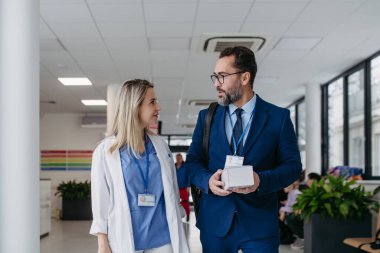 Tıp binasında doktorla konuşan ilaç satış temsilcisinin portresi. Takım elbiseli hırslı erkek satış temsilcisi yeni ilaç sunuyor..